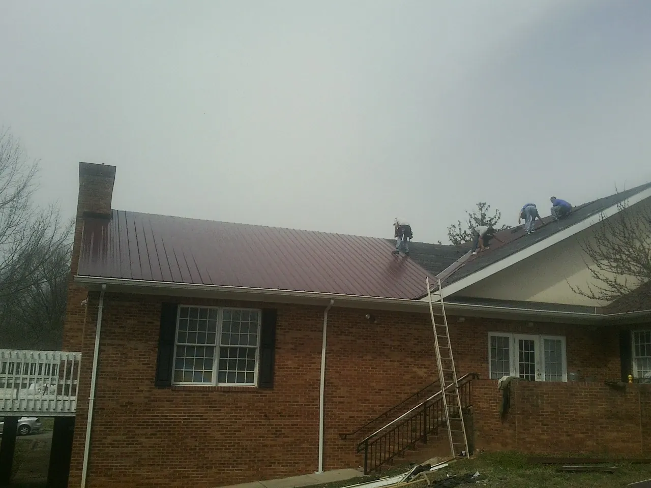 Crew setting red metal roofing panels on a brick home in Chalmette