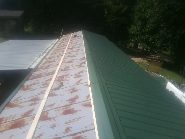 Old rusted panels beside newly installed green metal roofing — Wind Damage Roof Repair by Roofing Brothers in Chalmette