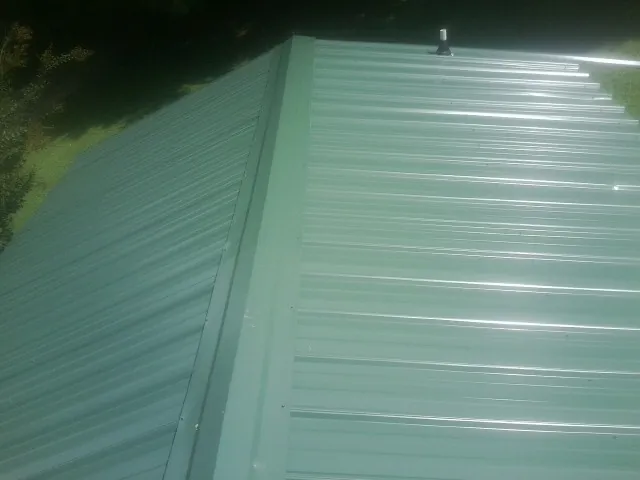 New green metal panels meeting at the ridge of a roof — Flat Roof Repair work by our crew in Chalmette